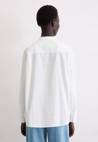 Biała koszula z długim rękawem z delikatnymi pionowymi paskami, mankietami na guziki i luźnym krojem. Gładka tkanina, zaokrąglony dół i klasyczny kołnierzyk.