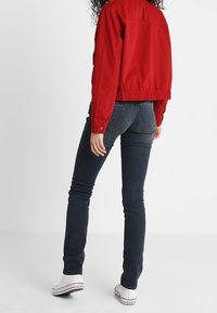 Rode cropped jas van katoen, gecombineerd met donkerblauwe jeans. De jeans hebben een slim fit, met subtiele stikseldetails, en witte sneakers.