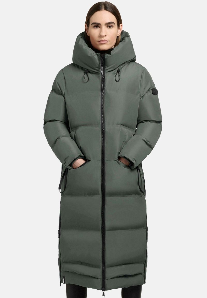 Cappotto lungo imbottito di colore verde scuro con colletto alto, zip frontale e tasche laterali. Presenta una texture liscia e raffinata e cappuccio con cordoncino.