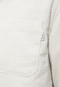 Világos bézs kordbársony dzseki függőleges csíkokkal, mellkasi zsebbel és egy kis "Pepe Jeans" feliratú címkével a bal oldalon.