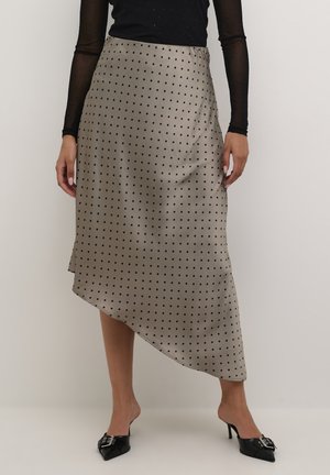 Falda asimétrica de satén beige con lunares negros, que presenta una textura suave y una abertura lateral. Combinada con mules negros de punta.