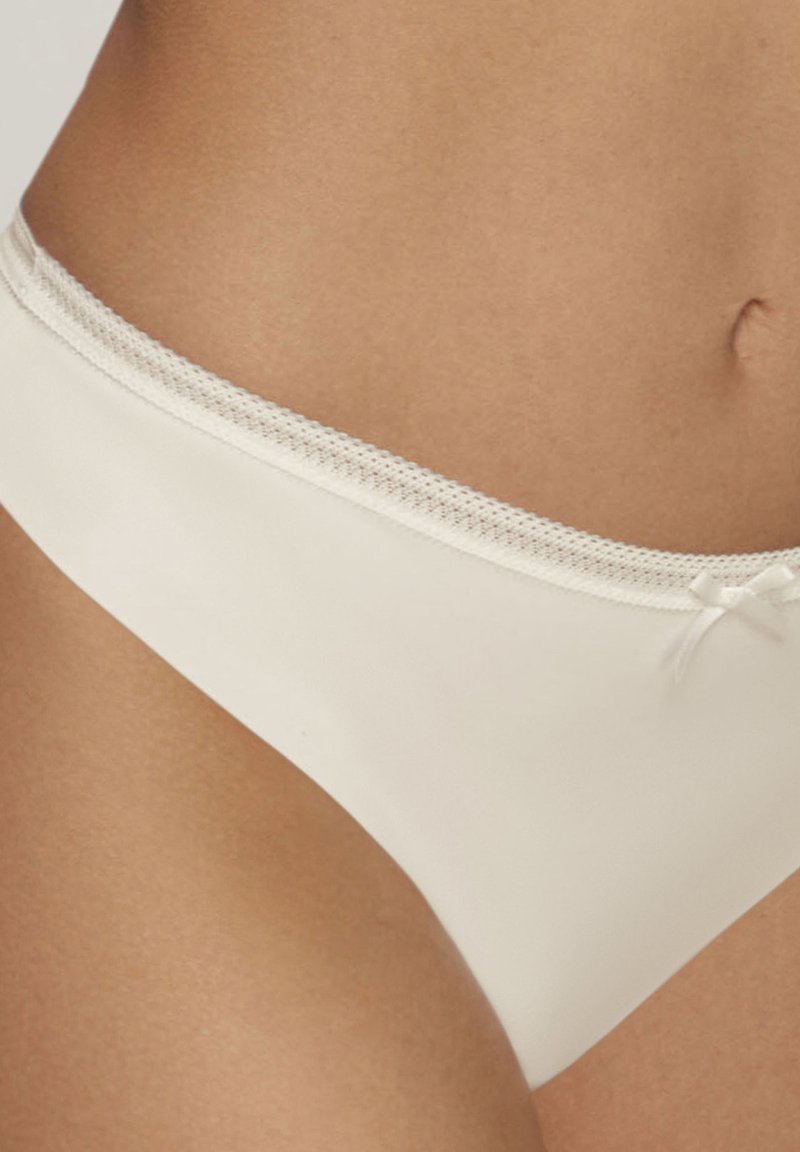 Sous-vêtements blancs sans couture avec une ceinture en dentelle texturée et un petit nœud sur le côté. Fini lisse sans coutures visibles.