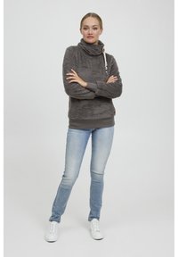 Grå fleece-tröja med hög krage och dragsko, kombinerad med ljusblå slim fit-jeans och vita sneakers. Slät textur, avslappnad passform.