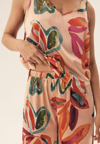 Zestaw piżamowy z satyny w jasnoróżowym kolorze, zdobiony żywymi wzorami liści w kolorach czerwonym, zielonym i niebieskim. Tank top ma dekolt w kształcie litery V; spodnie posiadają elastyczną talię.