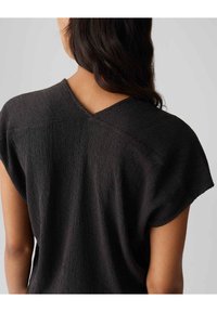 Top nero con texture, caratterizzato da uno scollo a V sul retro, maniche a cappuccio e una vestibilità rilassata. Il tessuto presenta un aspetto stropicciato per un tocco di stile in più.