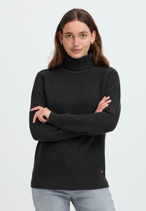 Pull en maille côtelée noir à col roulé avec des manches longues, texture tricotée et bord accentué. Porté sur un jean gris clair.