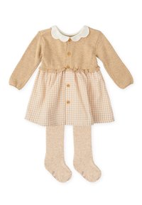 Vestido de punto en beige con un cuello blanco en forma de scallop, detalle de botones y una falda de cuadros; combinado con medias beige a juego.