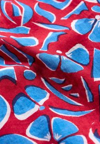 Röd tyg med ett blått och vitt abstrakt blommönster, med en mjuk yta och djärva, grafiska former genomgående.