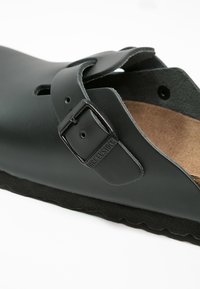 Sorte Birkenstock-sandaler med en glatt, matt overflate, justerbar spenne, korkfotseng og strukturert gummisåle.