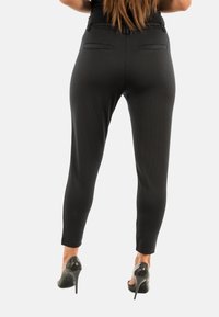 Pantalones negros a medida con un patrón de puntos, de corte ajustado y piernas entalladas. Cuenta con dos bolsillos traseros y se combinan con tacones altos negros brillantes.