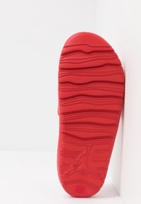 Punainen tennarin pohja, jossa on aaltoileva tekstuuripinta, sileät reunat ja keskeinen logo, joka esittelee kestävää kumimateriaalia.