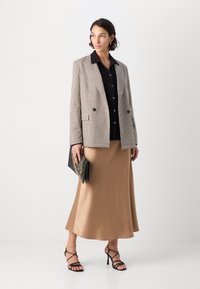 Beige ja musta ruuduline bleiser, must nööpidega särk, satiinist beež seelik, mustad rihmadega kontsad ja must käekott kuldse kettaktsendiga.