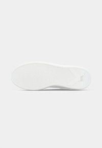 Suela de zapatillas blanca con patrones de surcos curvados y "KARL LAGERFELD" en relieve cerca del talón sobre un fondo gris claro liso.