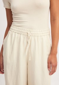 Kremlas elastīgas jostas bikses ar auklu, ar sānu kabatām un struktūrētu, vieglu audumu. Brīva piegriezuma.