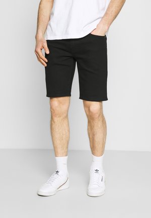 Shorts en denim noir avec une coupe droite, taille mi-hauteur, détails de couture subtils, portés avec un t-shirt blanc et des baskets blanches.
