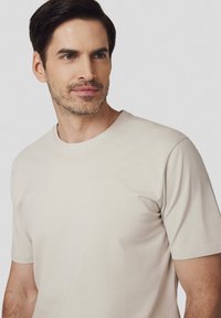 Beżowa bawełniana koszulka z okrągłym dekoltem i krótkimi rękawami. Gładka tekstura, dopasowany krój i minimalne detale przeszyć. Prosty design.