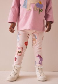 Pink long-sleeve shirt with a unicorn and flower design, paired with cream leggings featuring colorful unicorns and floral patterns. White high-top sneakers.