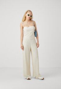 Débardeur en lin léger avec des bretelles spaghetti, associé à un pantalon large plissé en blanc cassé. Accessoirisé avec un sac bleu clair et des lunettes de soleil.