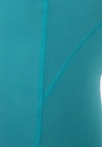 Close-up af turkis stof, der viser detaljerede dobbeltsyede sømme, der danner et vertikalt og diagonalt mønster.