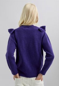 Suéter de punto morado con tela texturizada, que presenta hombros con volantes y mangas largas, terminado con un dobladillo acanalado.