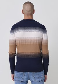Csíkos pulóver jumper barna, bézs és navy színek gradációjával. Kötött textúrával, bordázott mandzsettákkal és szegéllyel. Klasszikus kerek nyakú dizájn.