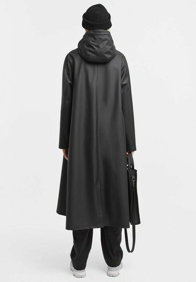 Zwarte waterdichte lange jas met een capuchon, gladde textuur en een relaxte pasvorm. Draagt het met donkere broeken en een zwarte handtas.