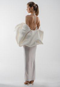 Balta satīna kleita ar augstu šķēlumu un plūstošu, pārmērīgi lielu apmetni. Ir haltera tipa kakla siksnas un gluda, spīdīga tekstūra.