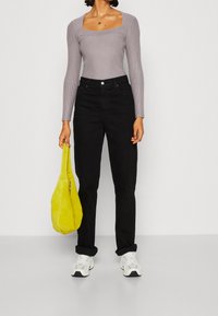 Graues, geripptes Langarmshirt, schwarze hochgeschnittene Jeans, knallgelbe Tasche und weiße Sneakers mit schwarzen Akzenten. Einfaches und modernes Outfit.