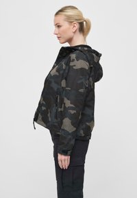 Camouflage jacket in shades of black and green, featuring a hood, zip front, and zippered pockets, made of textured synthetic material.