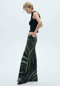 Zwarte geribbelde crop top gecombineerd met een lange groene rok met een patroon van bladeren, vloeiende stof en een slanke silhoutte.