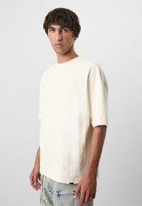 Crèmekleurig t-shirt met korte mouwen, een relaxte pasvorm en een ronde halslijn, gecombineerd met lichtblauwe versleten jeans.