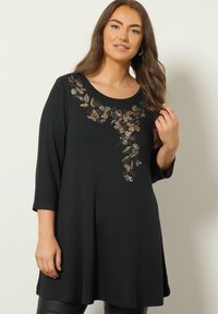 Tunika nera con maniche a tre quarti, caratterizzata da un design floreale in paillettes sul colletto. Tessuto morbido con una vestibilità rilassata.