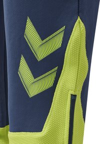 Marina idrottsbyxor med en texturerad limegrön detalj, försedd med diagonala chevronmönster i ljusgrön och en ficka med dragkedja.