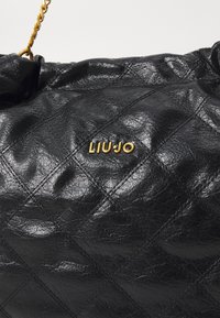 Bolsa de ombro sintética preta acolchoada com um logótipo dourado "LIU JO", um acabamento texturizado e uma alça de corrente para transporte.