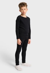 Svart långärmad topp och tajta leggings i mjukt tyg. Outfiten har en rund halsringning och en snug passform, i kombination med vita strumpor.