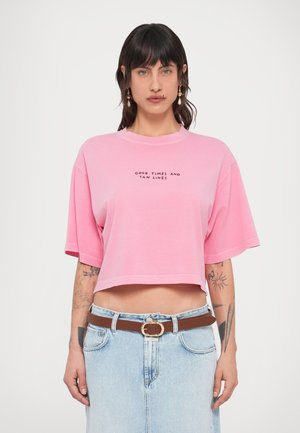 Ροζ κοντομάνικη cropped μπλούζα από απαλό ύφασμα με κοντά μανίκια, διακοσμημένη με μαύρο τυπωμένο κείμενο «GOOD TIMES AND TAN LINES.» Συνδυάζεται με τζιν φούστα.