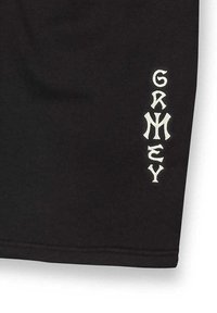 Zwarte shorts van een zachte stof, met witte geborduurde tekst "GRMZY" verticaal langs het linkerbeen. Eenvoudig ontwerp met strakke lijnen.