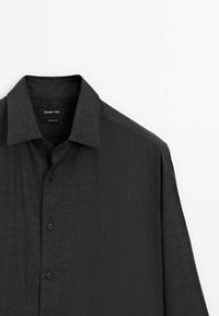 Chemise gris foncé à manches longues avec fines rayures verticales, boutonnée sur le devant et col classique, présentée sur fond blanc.