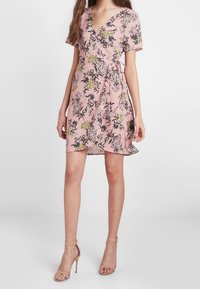 Robe courte rose à fleurs en cache-cœur avec des manches courtes, présentant un décolleté en V, un ourlet volanté et un détail noué à la taille.