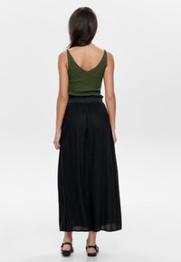 Grøn ærmeløs top og sort maxinederdel med løstsiddende pasform og taljebånd, med glat stoftekstur og subtile draperingsdetaljer.