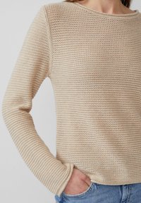 Beżowy sweter dziany o luźnym kroju, okrągłym dekolcie i długich rękawach. Posiada teksturowaną tkaninę z delikatnymi poziomymi paskami.