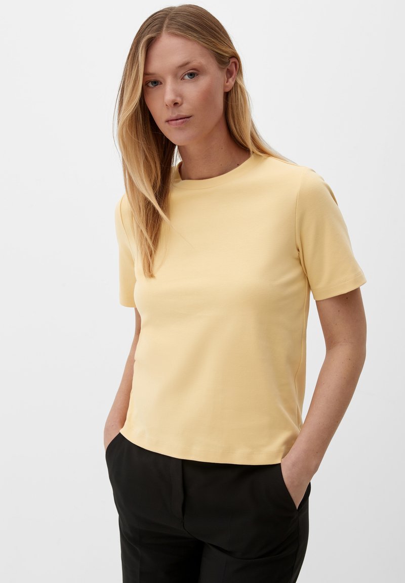 Geel T-shirt met korte mouwen en ronde hals, gemaakt van soepel katoen. Heeft een rechte zoom en een relaxte pasvorm. Gecombineerd met zwarte broek.