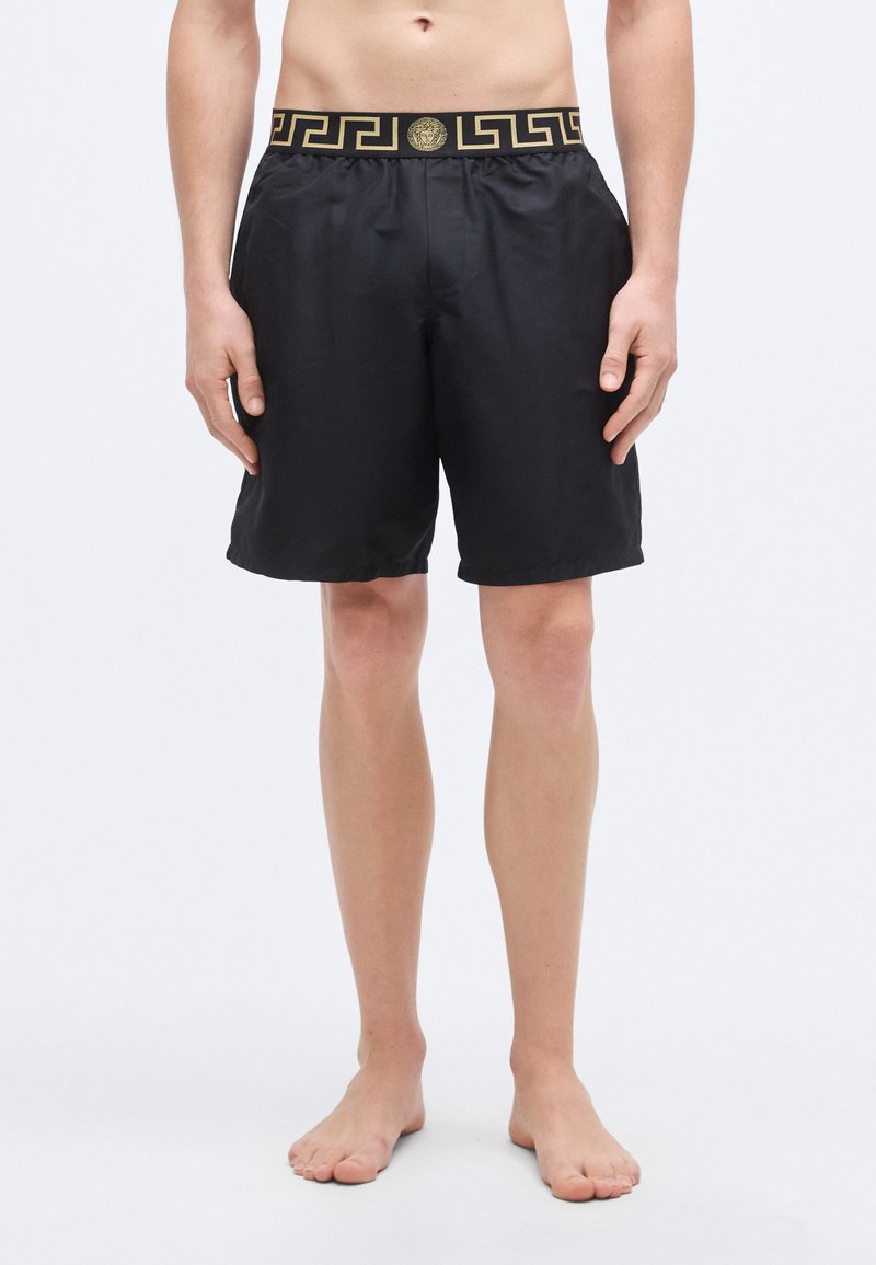 Zwarte zwemshort met een gouden Grieks sleutelmotief op de elastische tailleband. Gemaakt van lichtgewicht materiaal, met een eenvoudig, vlak ontwerp.