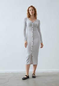 Gray ribbed midi dress with long sleeves, V-neck, and front buttons. Features a split at the hem, worn with dark flat shoes. Simple design.