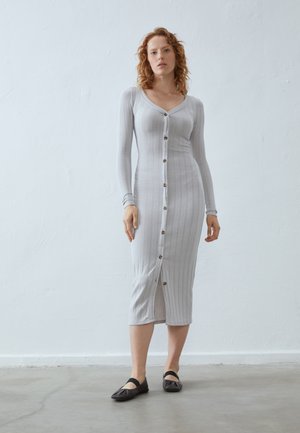 Gray ribbed midi dress with long sleeves, V-neck, and front buttons. Features a split at the hem, worn with dark flat shoes. Simple design.