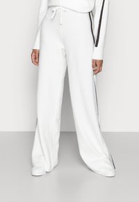 White wide-leg trousers made of soft, textured fabric. Features side stripes with a metallic sheen and an elastic waistband with drawstring.