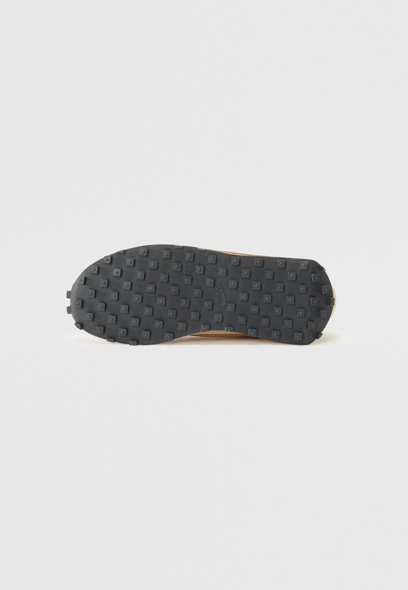 Semelle de chaussure en caoutchouc noir avec un motif texturé de carrés et de cercles, comportant de petites luges pour une traction. Pas de marque ou de détails visibles.