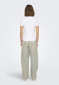 Camiseta blanca de manga corta con pequeños patrones cortados, combinada con unos pantalones vaqueros de pierna ancha en beige claro, que muestran un ajuste relajado.