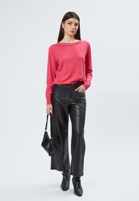 Roze langemouwen top met een bedekte halslijn, gecombineerd met zwarte leren wijde broek en zwarte enkellaarzen. Handtas met zwart patroon.