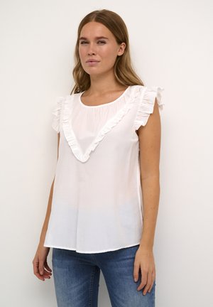 Top bianco senza maniche con dettagli a volant attorno al collo, caratterizzato da una vestibilità ampia e una texture morbida, abbinato a jeans azzurri chiari.